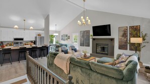 Eine moderne Küche mit weißen Schränken, ein Essbereich mit Tisch und Stühlen, ein Wohnzimmer mit einem grünen Sofa und ein Kamin.