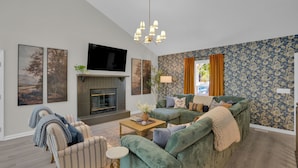 Ein Wohnzimmer mit Kamin, grünen Sofas, gestreiften Sesseln und einem Flachbildfernseher.