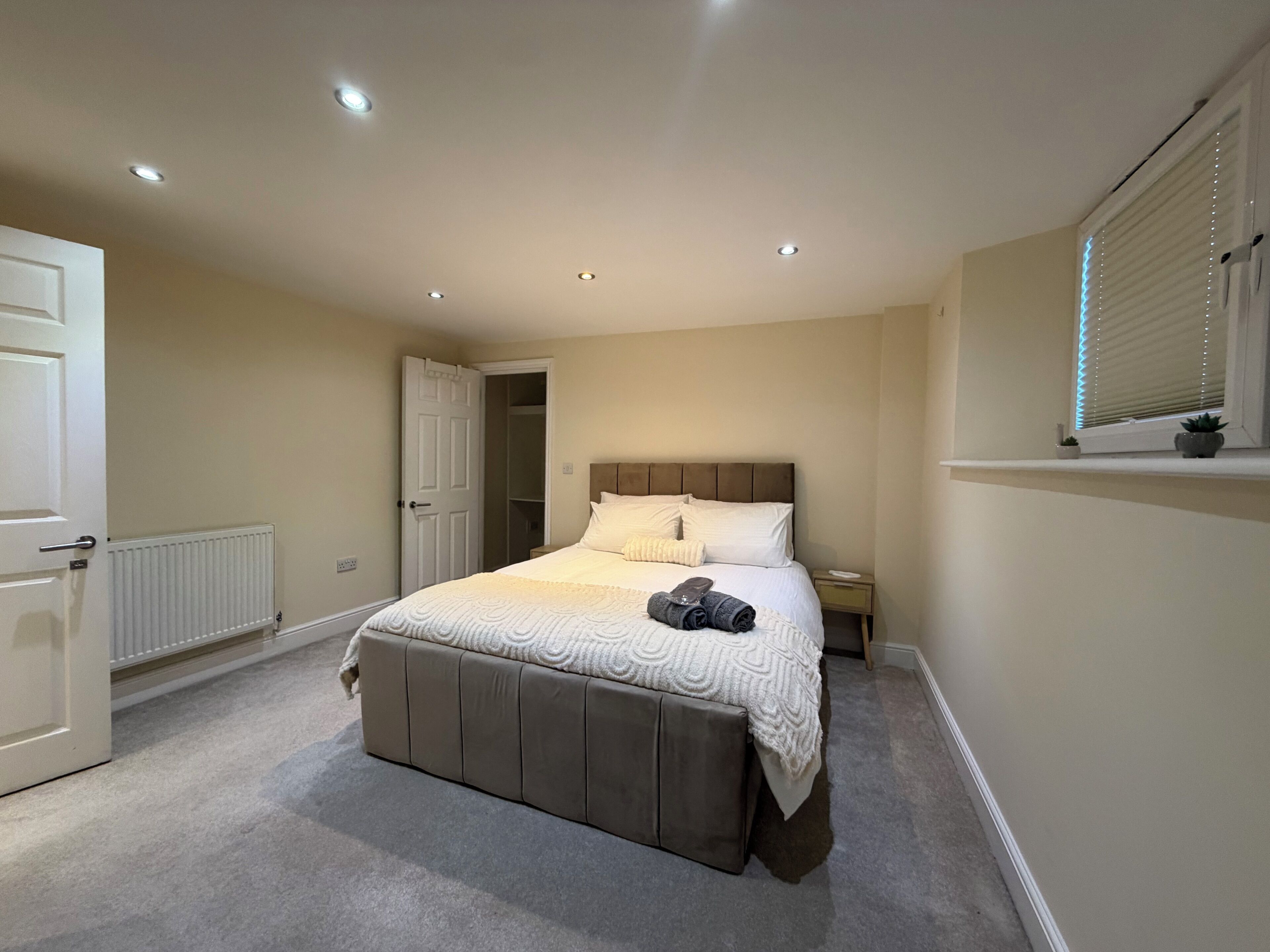 A bedroom with a bed, a radiator, a closet, a window with blinds, and a small plant on the windowsill.
