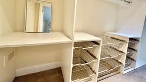Habitació amb paret blanca, un mirall i prestatges metàl·lics.