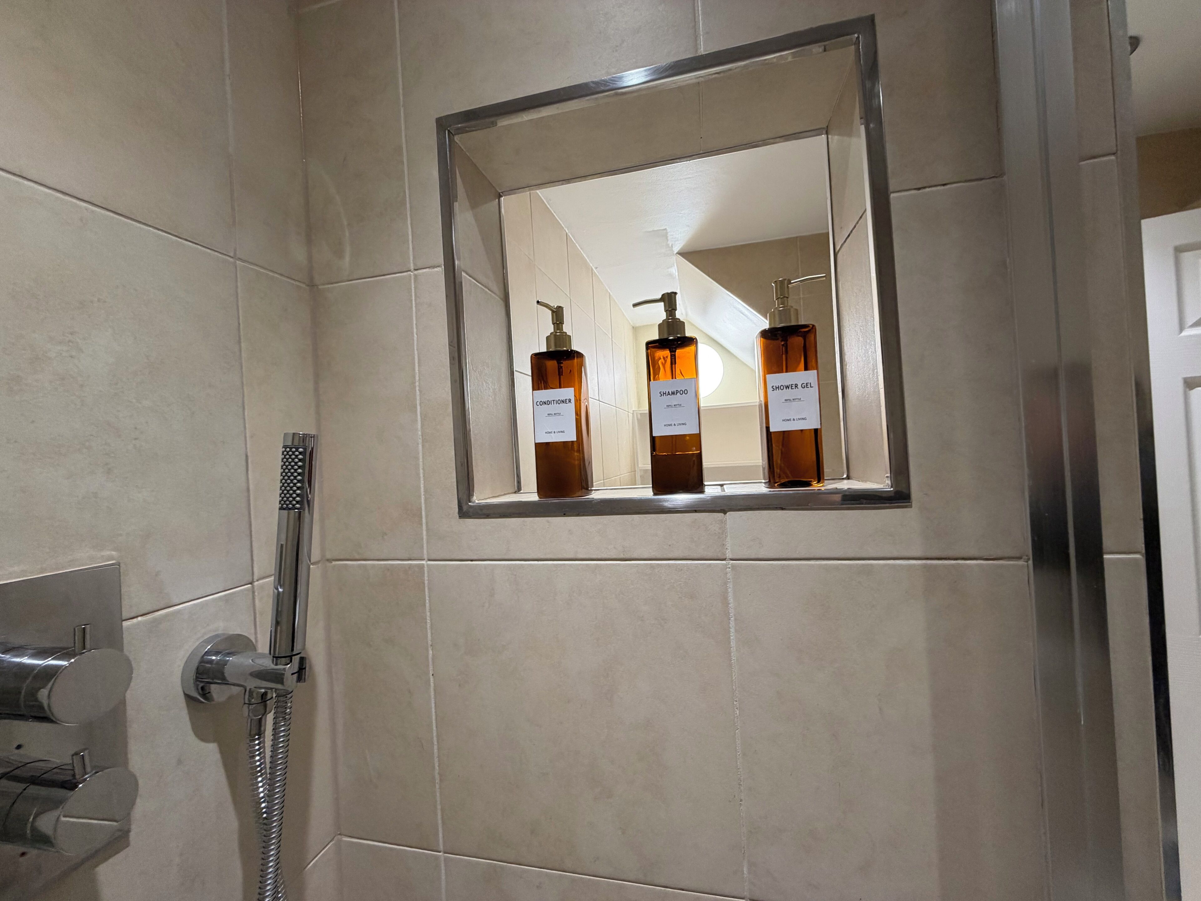 Une salle de bain équipée d’une douche, d’un sèche-mains et de deux flacons de produits de toilette.
