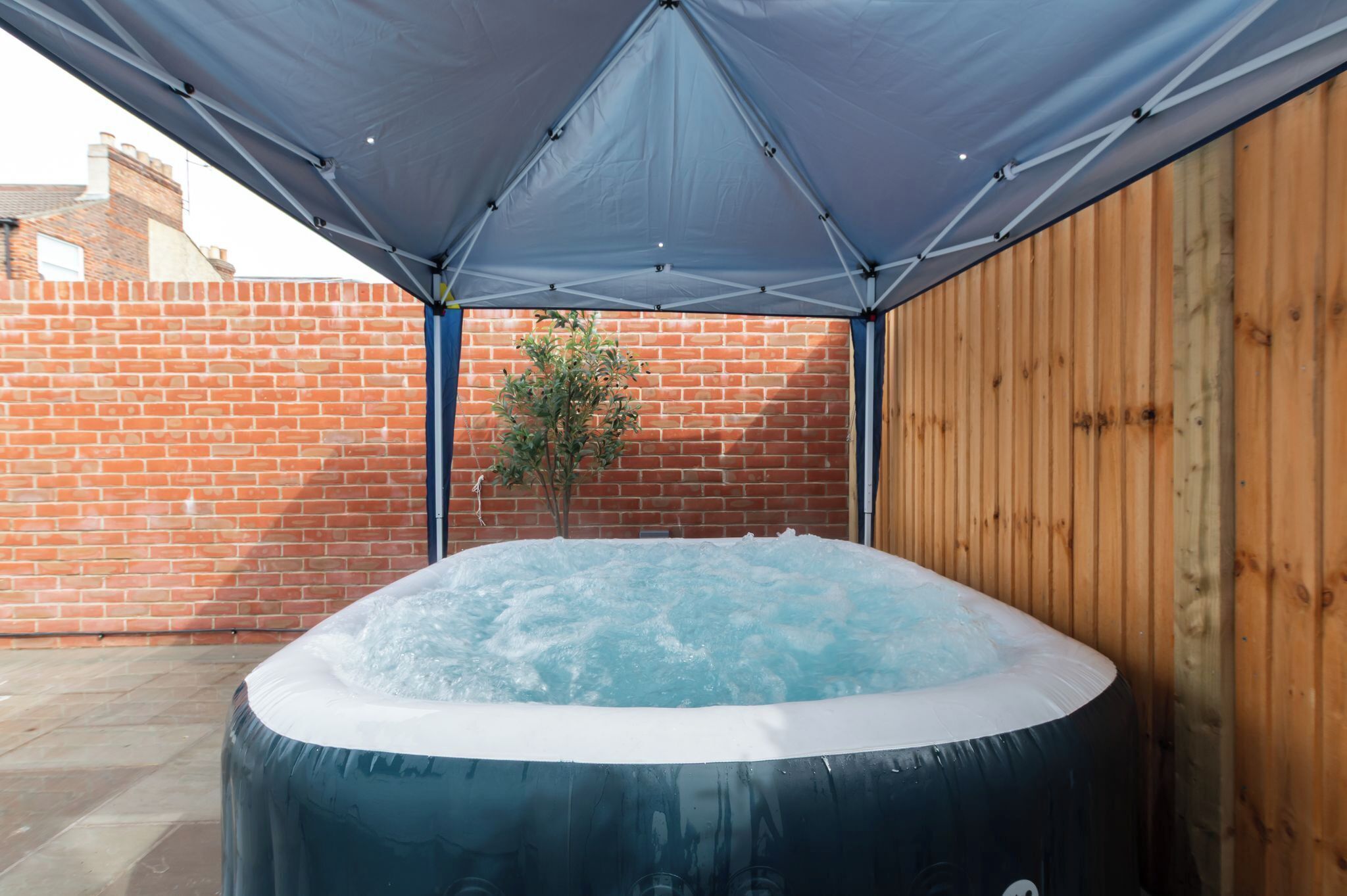 A hot tub under a canopy, surrounded by a brick wall and wooden fence.