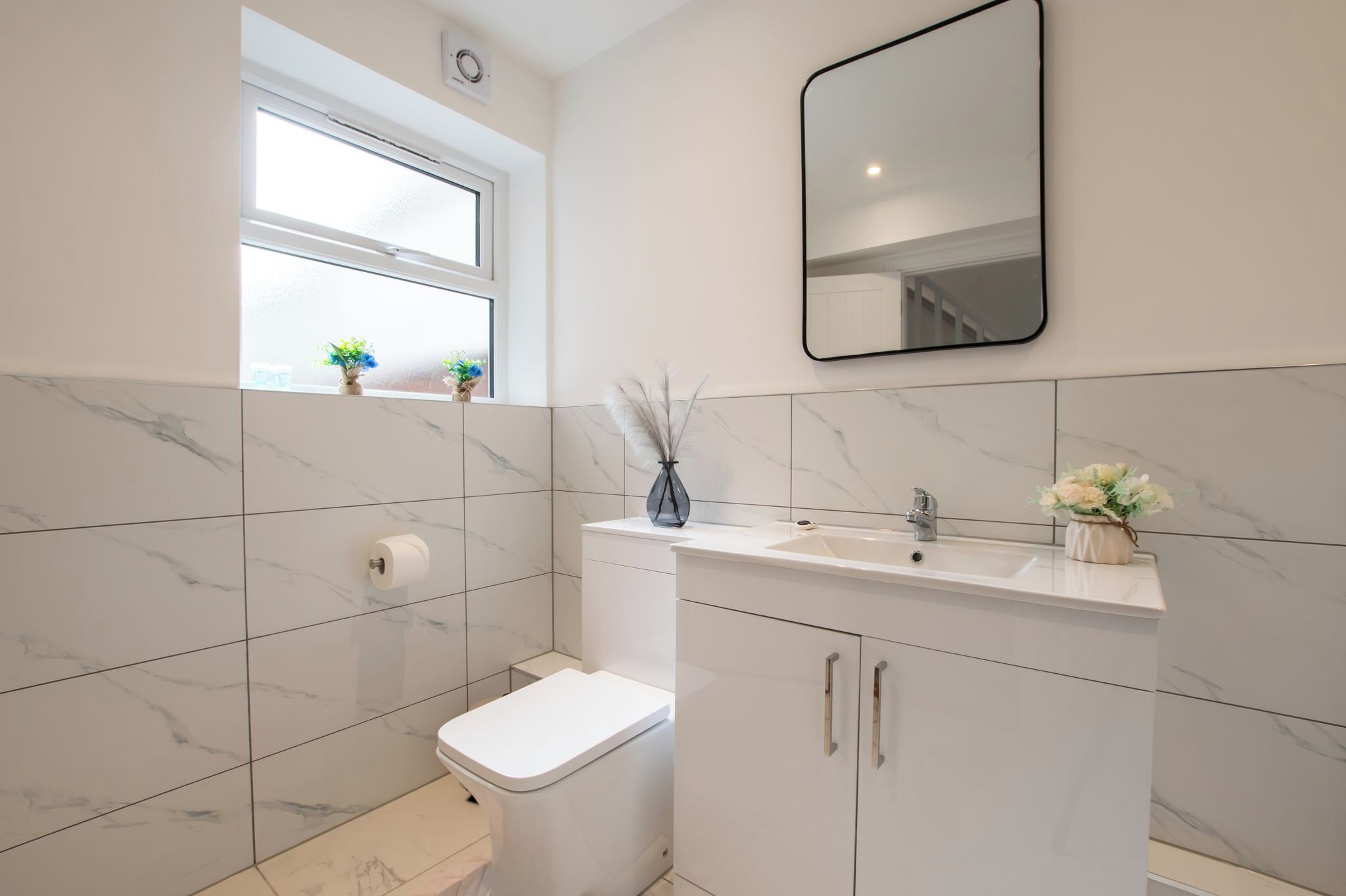 Et moderne badeværelse med toilet, vask, spejl og vindue.
