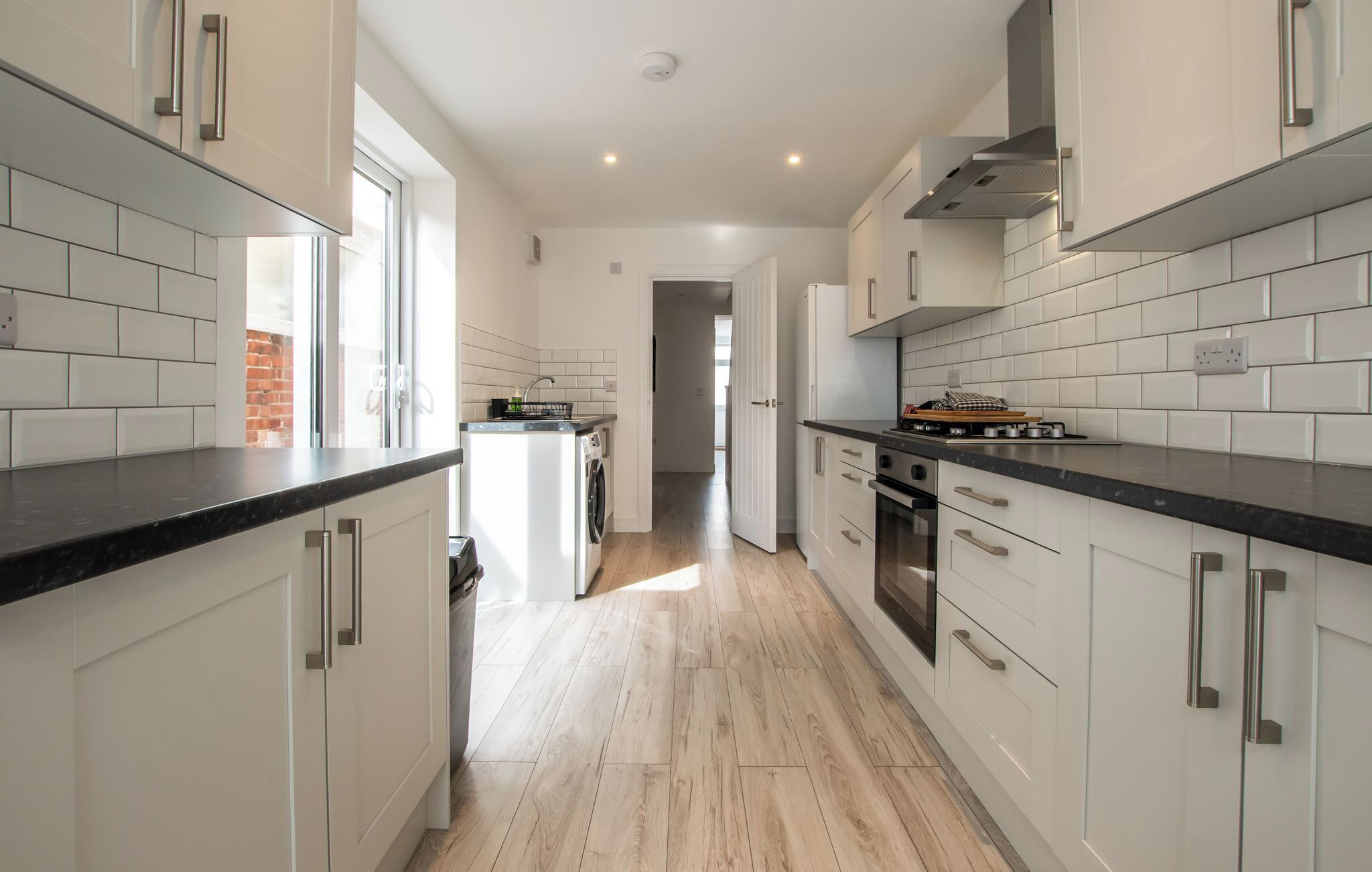 Una cocina moderna con piso de madera clara, armarios blancos y electrodomésticos de acero inoxidable.