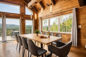 A wooden interior with a dining table, chairs, and large windows offering a view of the outdoors. - Spa, Pool Table & Nature | Les Bons Vivants (Saint-Côme)