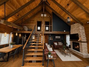 A spacious loft with a high ceiling, a central staircase, a stone fireplace, and a cozy seating area. - Spa, Pool Table & Nature | Les Bons Vivants (Saint-Côme)
