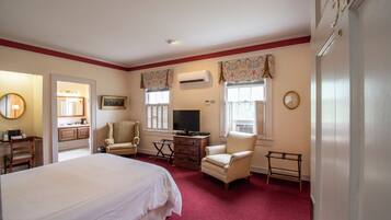 A hotel room with a large bed, two armchairs, a television, a dresser, and an air conditioning unit.