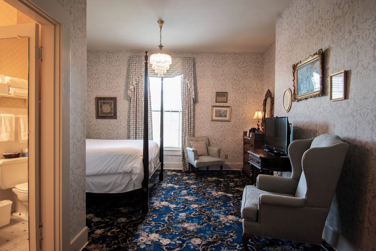 Una habitación de hotel con cama, una silla, televisor y escritorio.