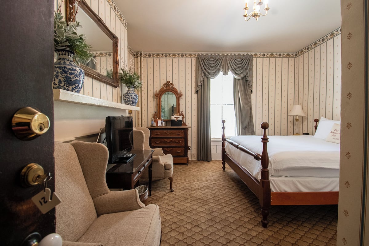 Una habitación de hotel con una cama, televisión, cómoda, silla, espejo y una planta en maceta.