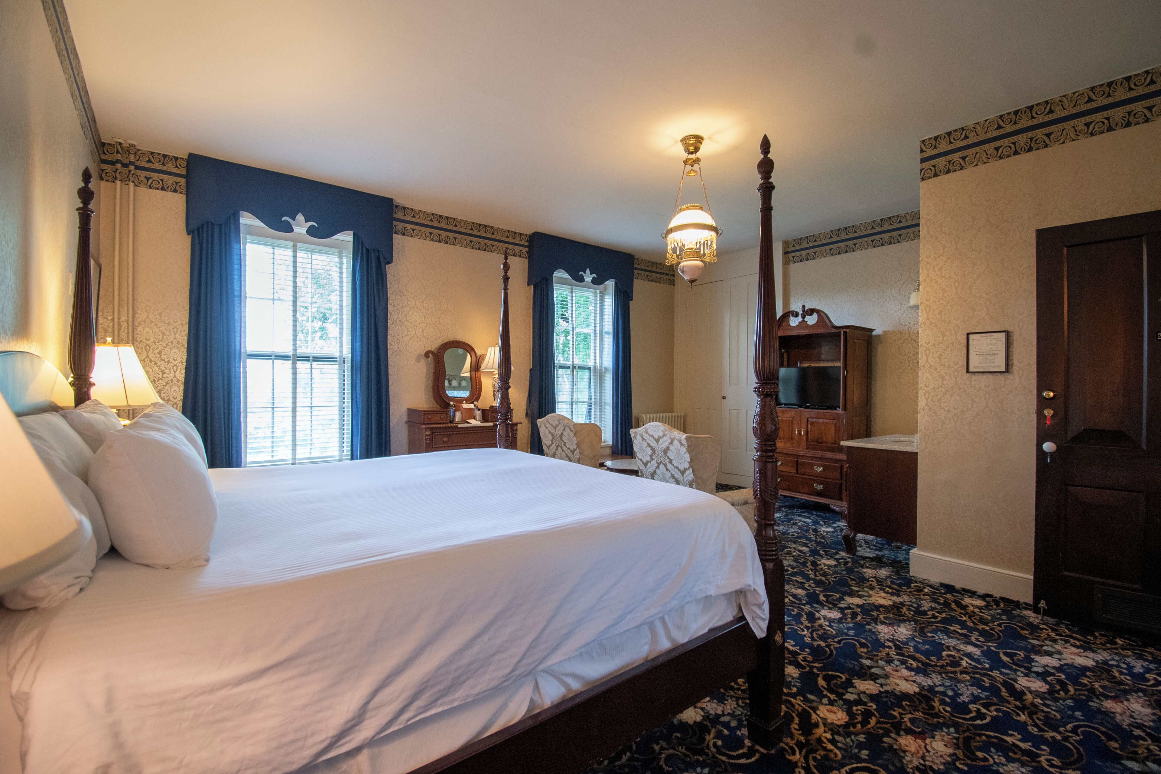 A four-poster bed, a wooden dresser, a mirror, and a chandelier in a hotel room.