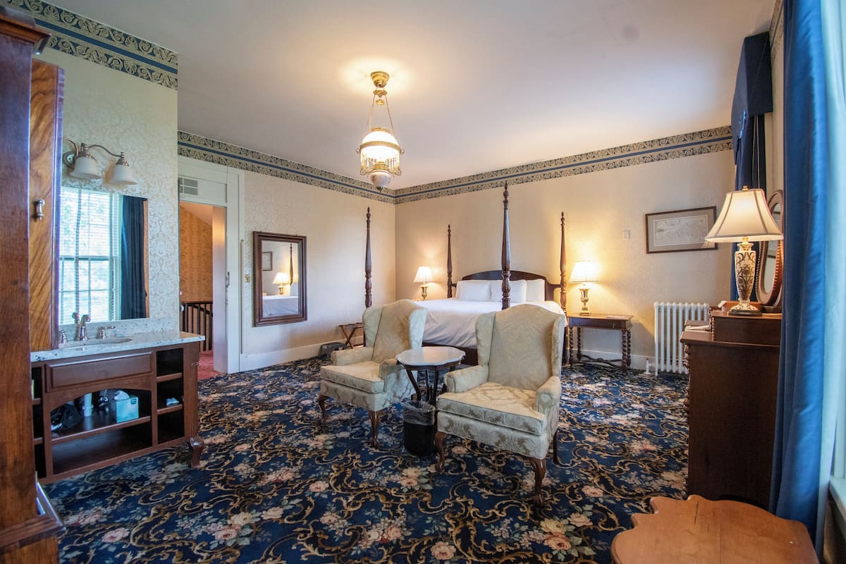 Habitación de hotel con cama, dos sillones, una mesita, espejo, radiador y candelabro.