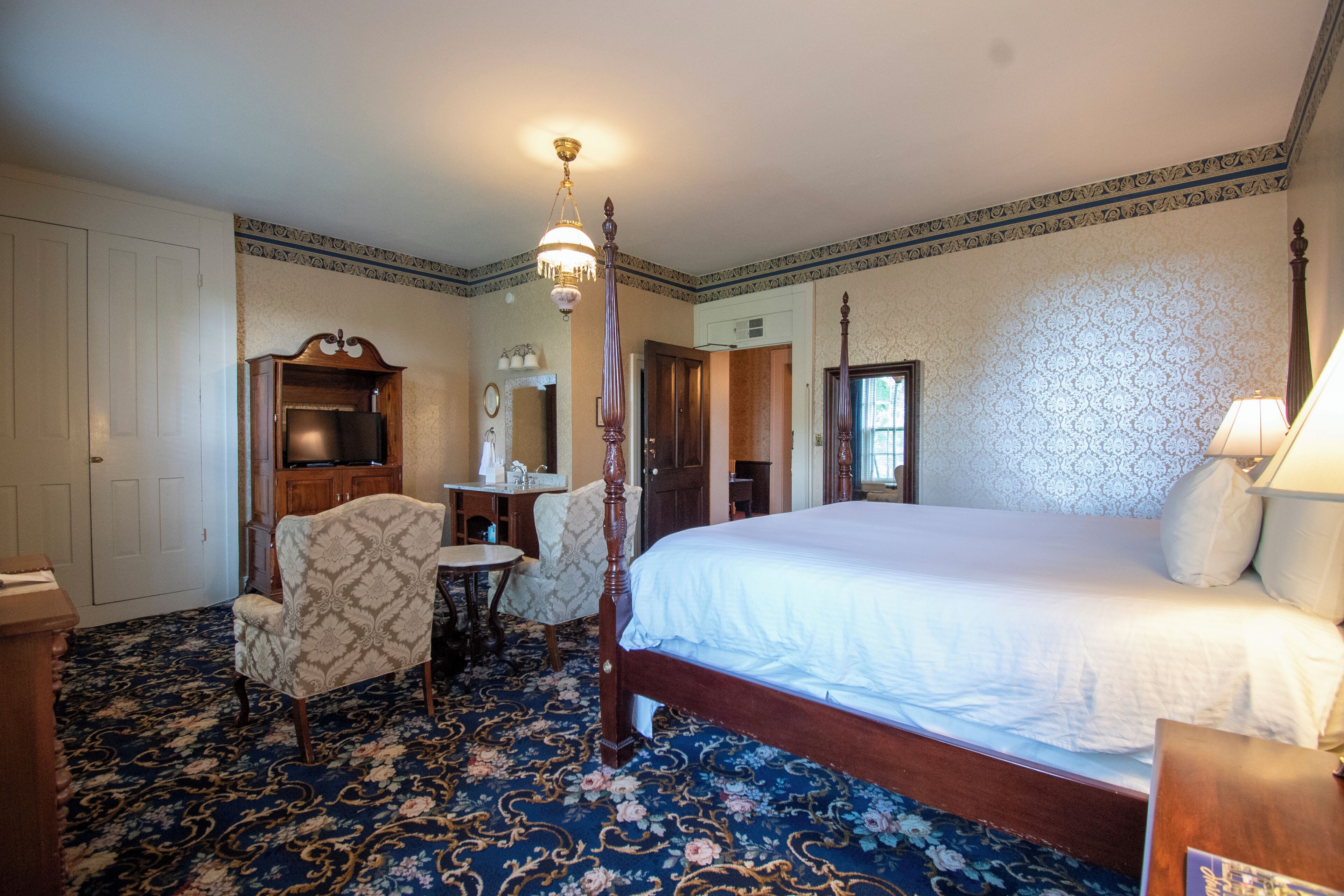 A bedroom with a large bed, a desk, a chair, a vanity, and a chandelier.