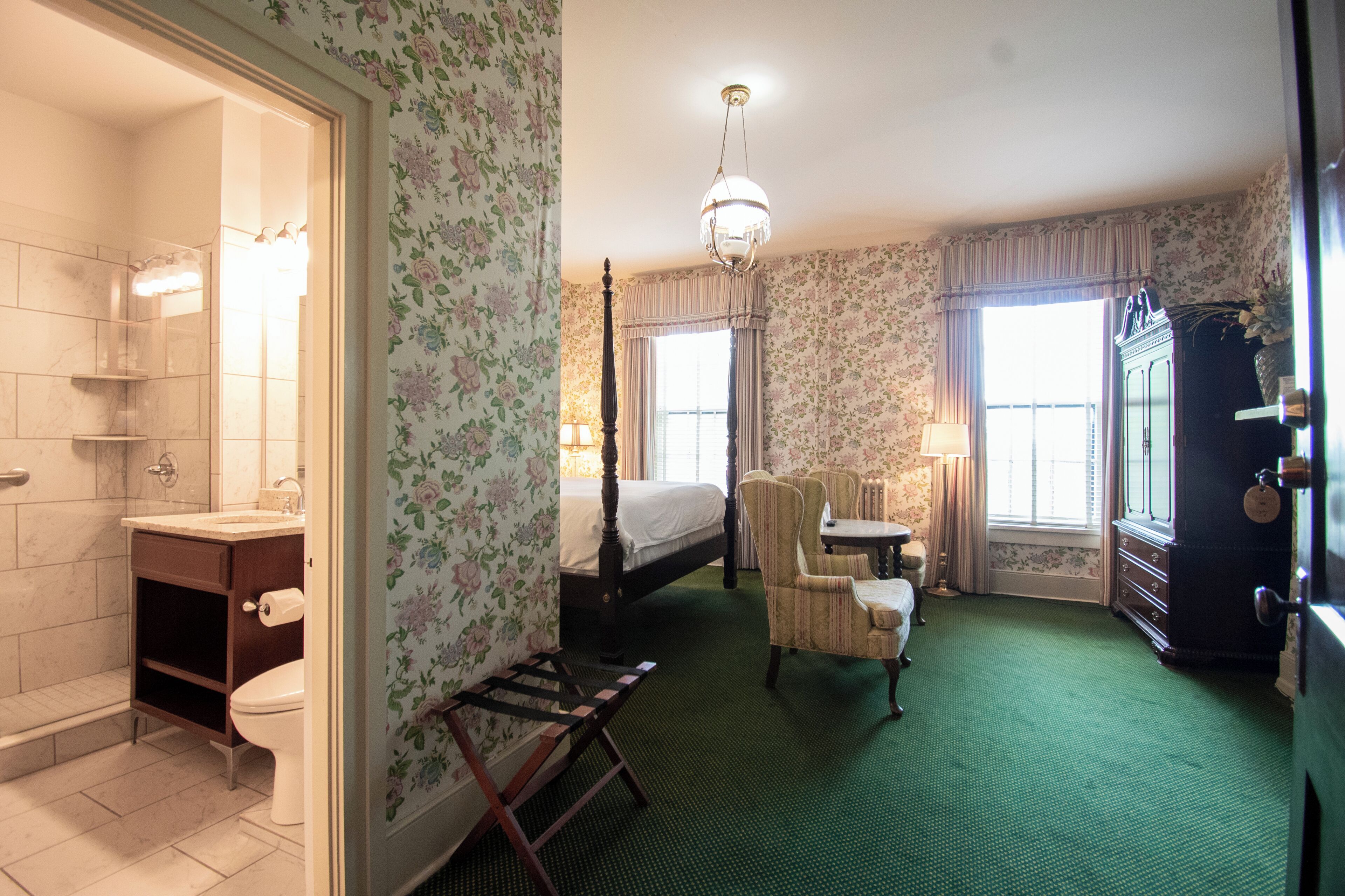 A hotel room with a bathroom, a bed, a chair, a dresser, and a window.