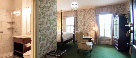 A hotel room with a bathroom, a bed, a chair, a dresser, and a window.