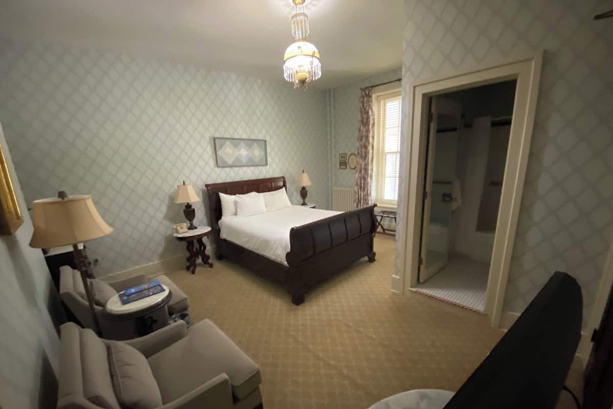 Habitación de hotel con una cama, un escritorio, una silla, una lámpara, un reloj y una puerta que da a un baño.