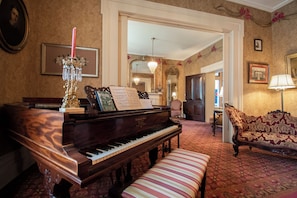 A grand piano, a bench, a patterned sofa, a chandelier, and a mirror in a room with ornate wallpaper and a carpeted floor. - Beaumont Inn (Harrodsburg)