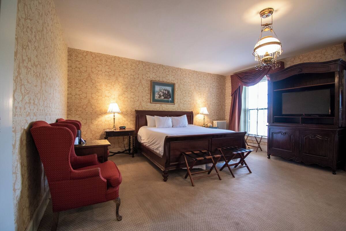 Una habitación de hotel con cama, escritorio, silla, televisor y lámpara.