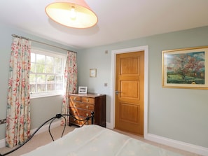 A bedroom with a bed, a dresser, a door, a window with curtains, a ceiling light, and a framed picture on the wall. - Ormiston House (Pewsey)