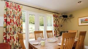 A dining area with a wooden table, chairs, and a window with curtains. - Ormiston House (Pewsey)