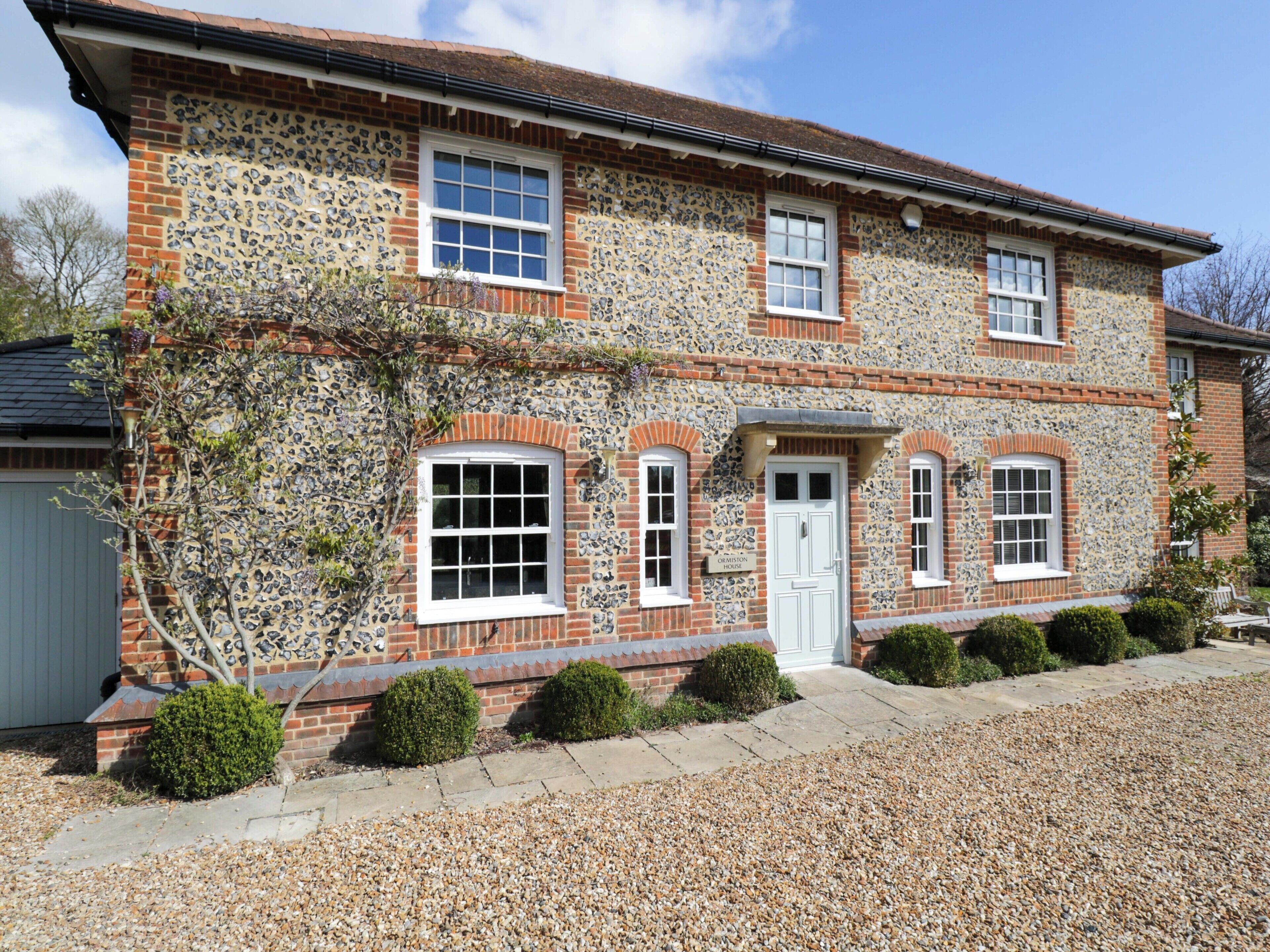A stone house with a white door, multiple windows, and a gravel driveway.