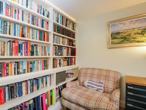 A room with a bookshelf filled with books, a plaid armchair with a cushion, and a painting on the wall. - Ormiston House (Pewsey)
