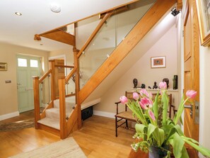 A wooden staircase with a glass balustrade, a green door, a chair, and a vase of flowers. - Ormiston House (Pewsey)