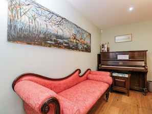 Una habitación con un sofá rojo, un piano de madera y un cuadro abstracto grande en la pared.
