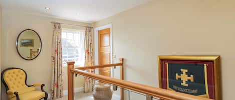 Una escalera con barandilla de madera, un sillón amarillo, una cesta de mimbre, un cuadro enmarcado y un espejo en la pared.