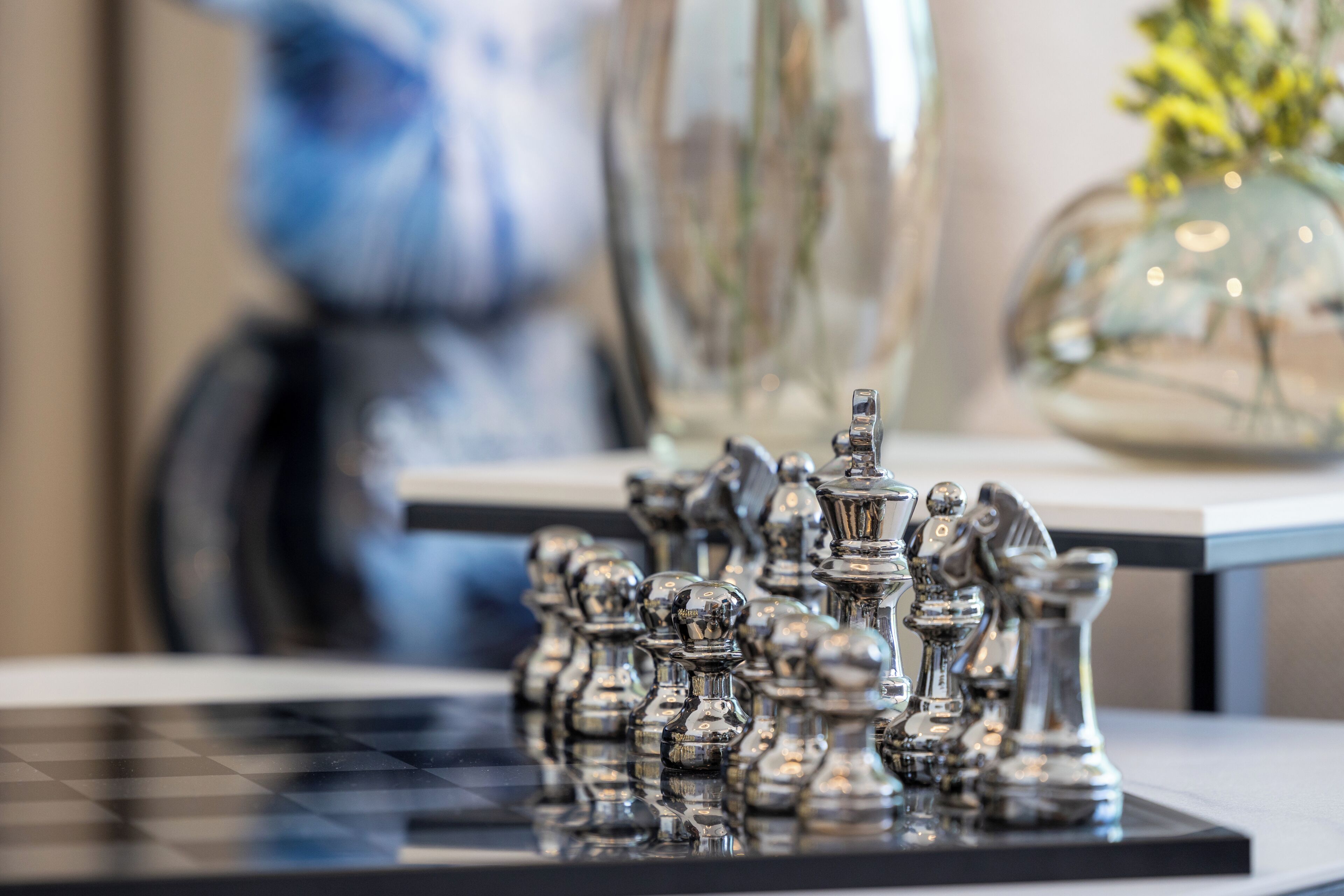 A chessboard with chess pieces, a vase with flowers, and a blurred painting in the background.