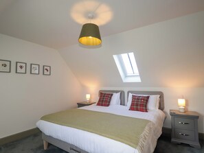 Une chambre à coucher avec un lit, des tables de chevet, une lucarne et des tableaux encadrés accrochés au mur.
