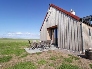 Una stalla di legno con tetto rosso, un patio con sedie e vista su un campo verde.