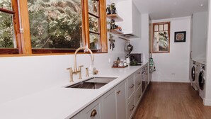Une cuisine avec un plan de travail blanc, des armoires en bois, un évier et une fenêtre donnant sur un paysage verdoyant.
