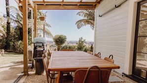 Un espace extérieur abrité, aménagé pour les repas, avec une table et des chaises en bois, un barbecue et une vue sur le paysage.