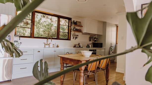 Une cuisine avec des meubles blancs, une table en bois et une fenêtre donnant sur un paysage verdoyant.