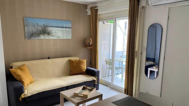 A room with a sofa, a small table, a mirror, and a sliding glass door leading to an outdoor area. - STUDIO LE FLAMANT 20M FROM THE BEACH (Palavas-les-Flots)