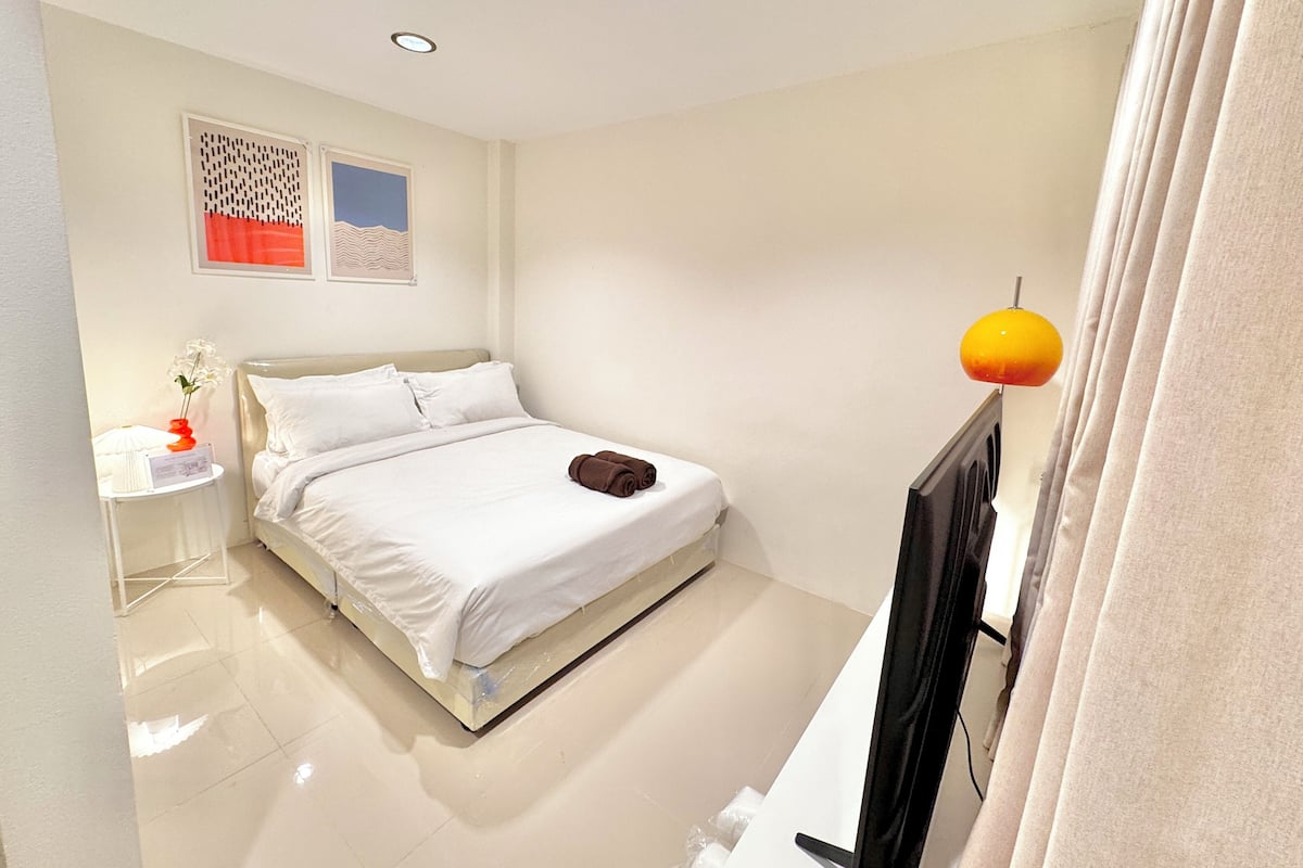 Une chambre d’hôtel moderne, équipée d’un lit, d’une table de chevet, d’une lampe et d’un tableau au mur.