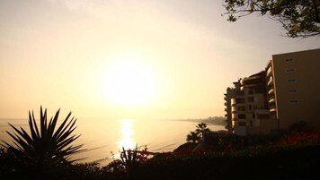Un edificio de varios pisos, con un balcón y vista al mar durante la puesta de sol.
