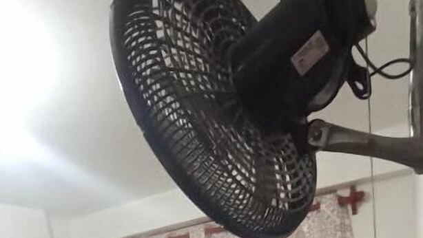 Een hotelkamer met een bed, nachtkastje, lamp en plafondventilator.