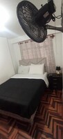Una habitación de hotel con cama, mesita de noche, lámpara y ventilador de techo.