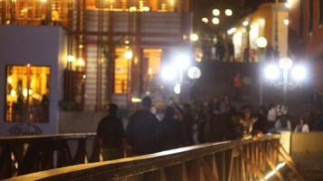 Un espacio al aire libre concurrido, con barandilla, posiblemente un puente o pasarela, y edificios al fondo.