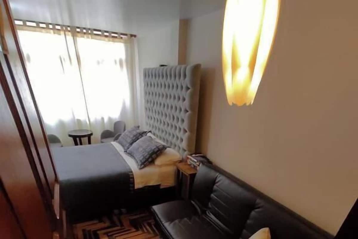 Une chambre à coucher comprenant un lit, un canapé, un tapis à motifs et un luminaire fixé au mur.