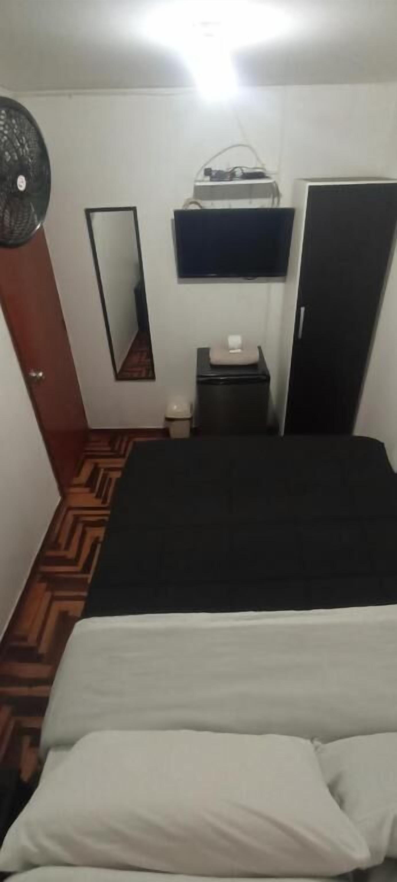 Una camera da letto con un letto, una cassettiera, uno specchio, una TV e una ventola.