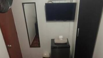 Una camera da letto con un letto, una cassettiera, uno specchio, una TV e una ventola.