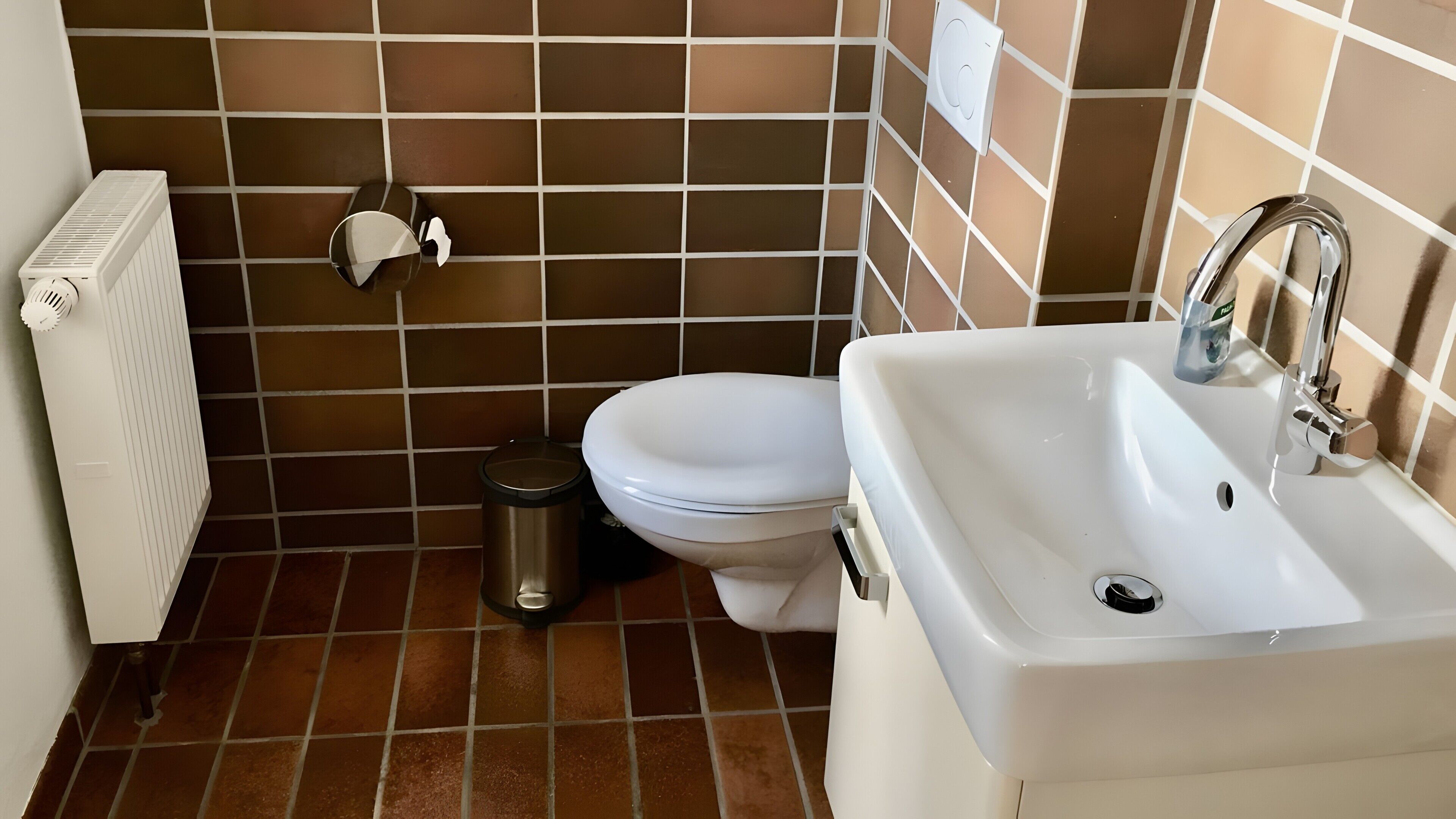 Ein Badezimmer mit Toilette, Waschbecken, Mülleimer, Radiator und Wandheizung.