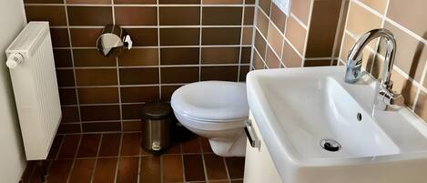 A bathroom with a white toilet, a sink, a trash bin, a radiator, and a wall-mounted heater.