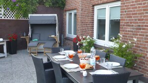 En udendørs terrasse med spisebord dækket til fire personer, omgivet af fletstole.
