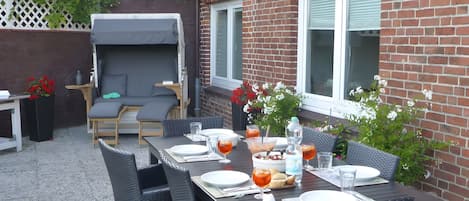 En udendørs terrasse med spisebord dækket til fire personer, omgivet af fletstole.