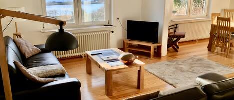 Un salon avec un canapé, une table basse, un téléviseur et une vue sur un paysage enneigé par les fenêtres.