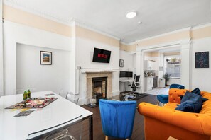 Ein modernes Wohnzimmer mit Kamin, einem Essbereich mit Gesellschaftsspiel und einer Küche im Hintergrund.