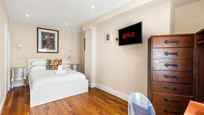 Un dormitorio con una cama, un aparador de madera, un televisor y un cuadro en la pared.